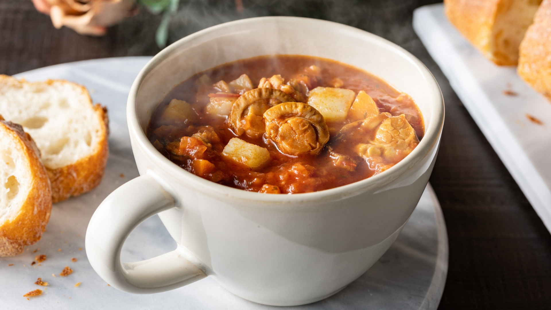 Hot soup in a mug with sliced bread on the side.