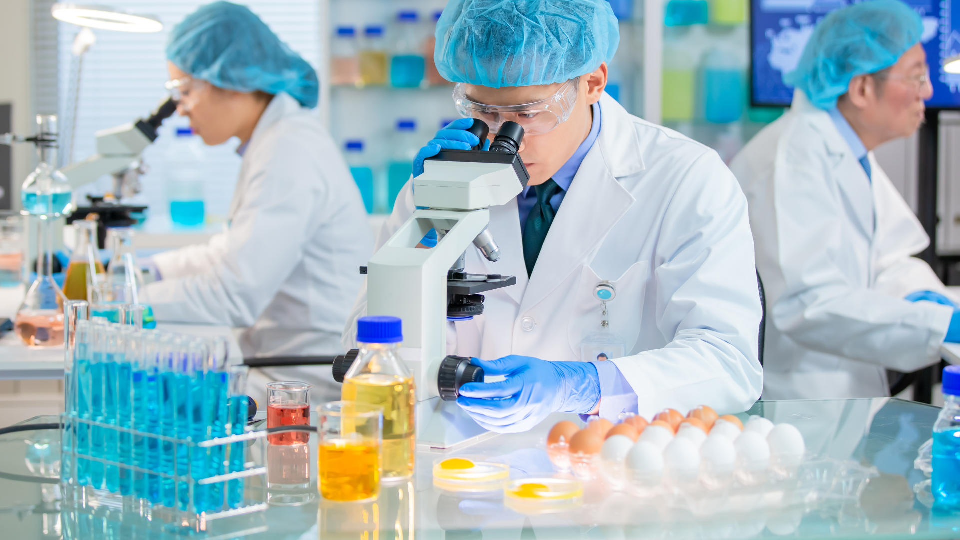 Scientists in lab coats examining samples under a microscope.