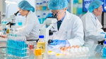 Scientists in lab coats examining samples under a microscope.