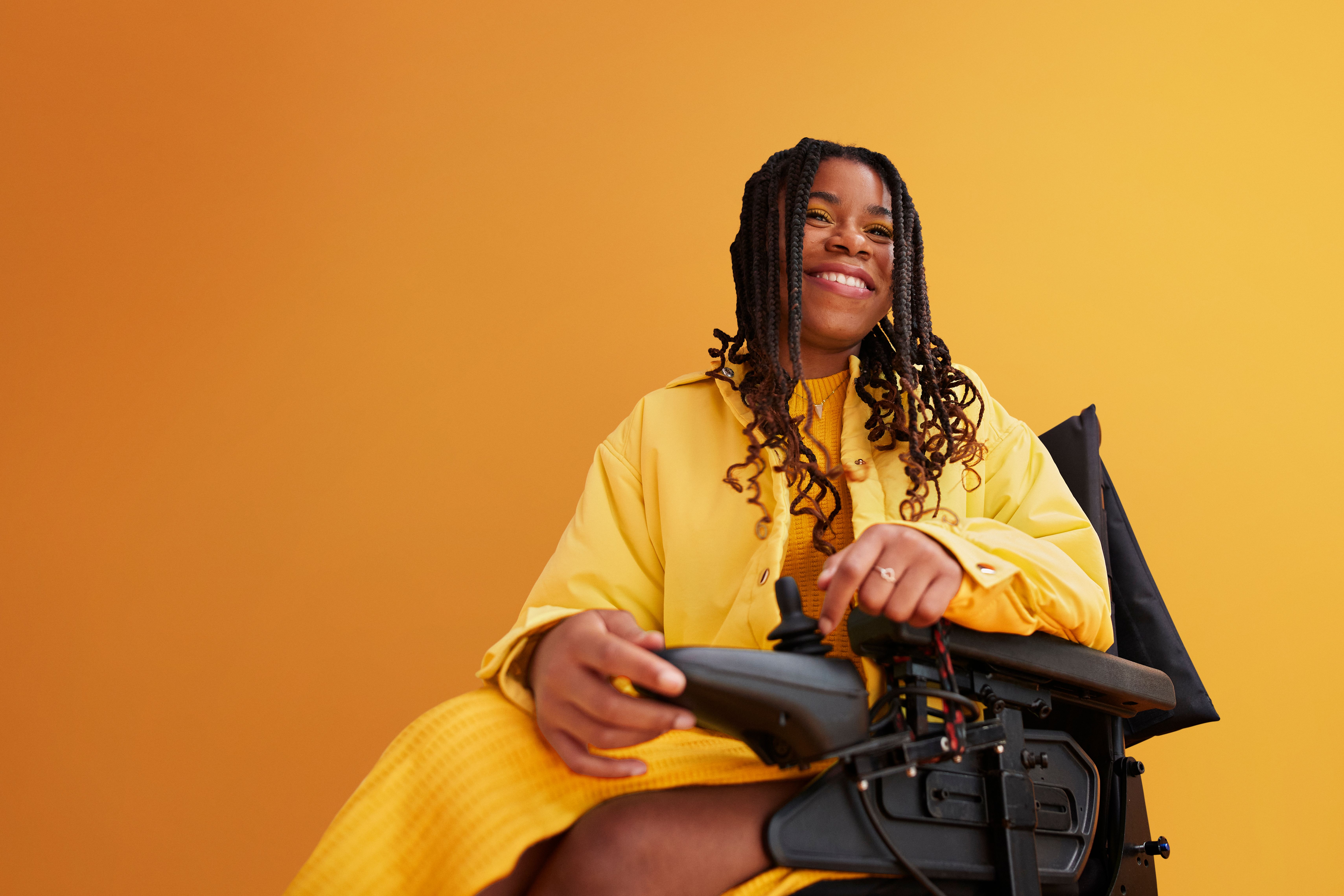 Smiling woman in a wheelchair, wearing a yellow top in front of a yellow background