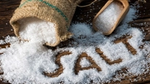 Coarse salt spilled from burlap sack with salt written on wooden surface.