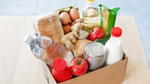 A cardboard box filled with food items, including milk, eggs, bread, ginger and tomatoes.