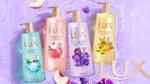 Four bottles of Lux Sparkling shower gel. One pink, one gold, one turquoise and one lilac, on a purple background with peach slices.