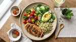 Grilled chicken with quinoa, mixed vegetables, and avocado salad on a wooden table with herbs and spices.