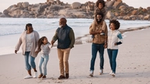 Family walking on a sandy beach with rocky background.