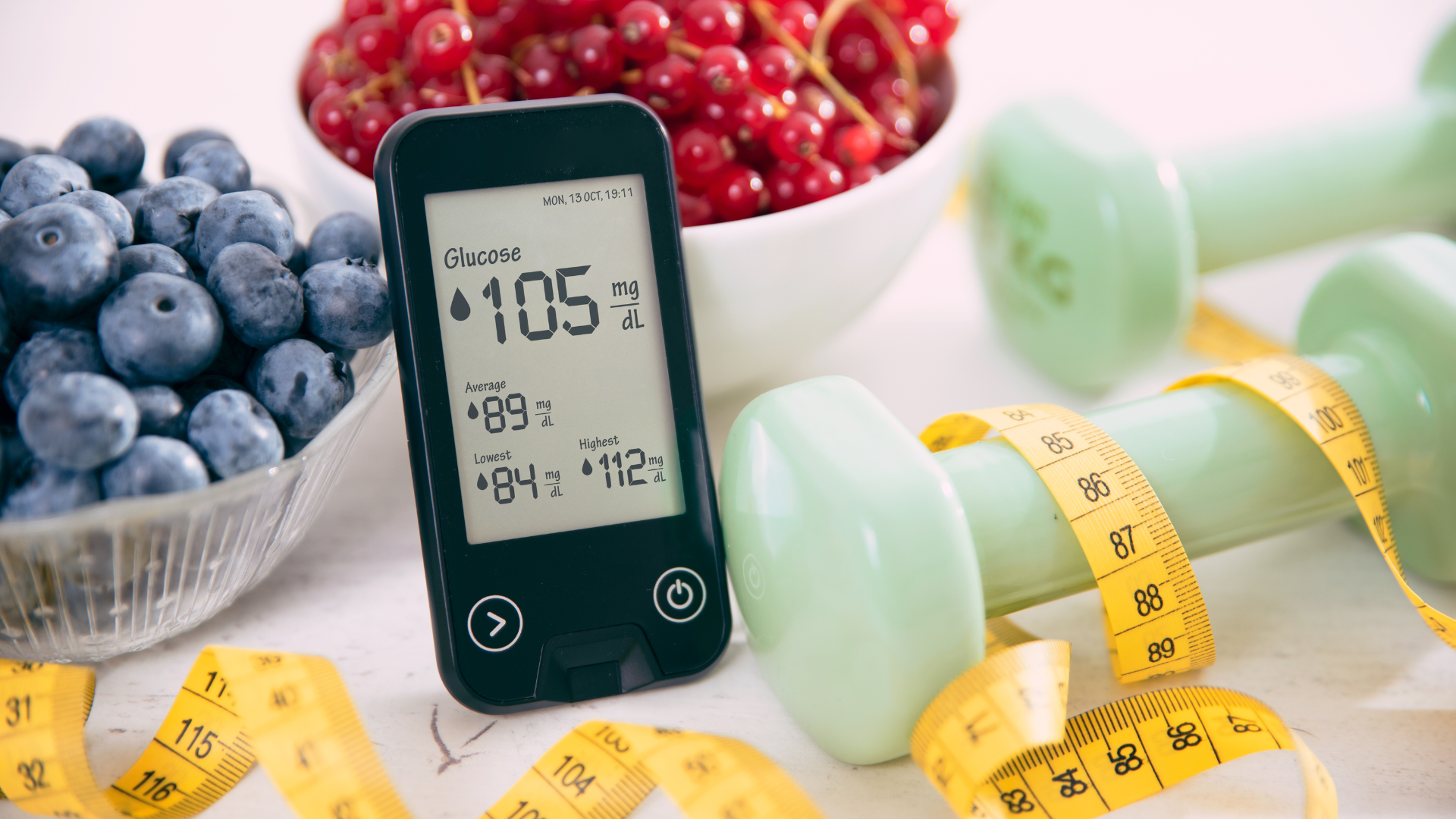 Glucose meter with blueberries, red currants, green dumbbells, and tape measure.