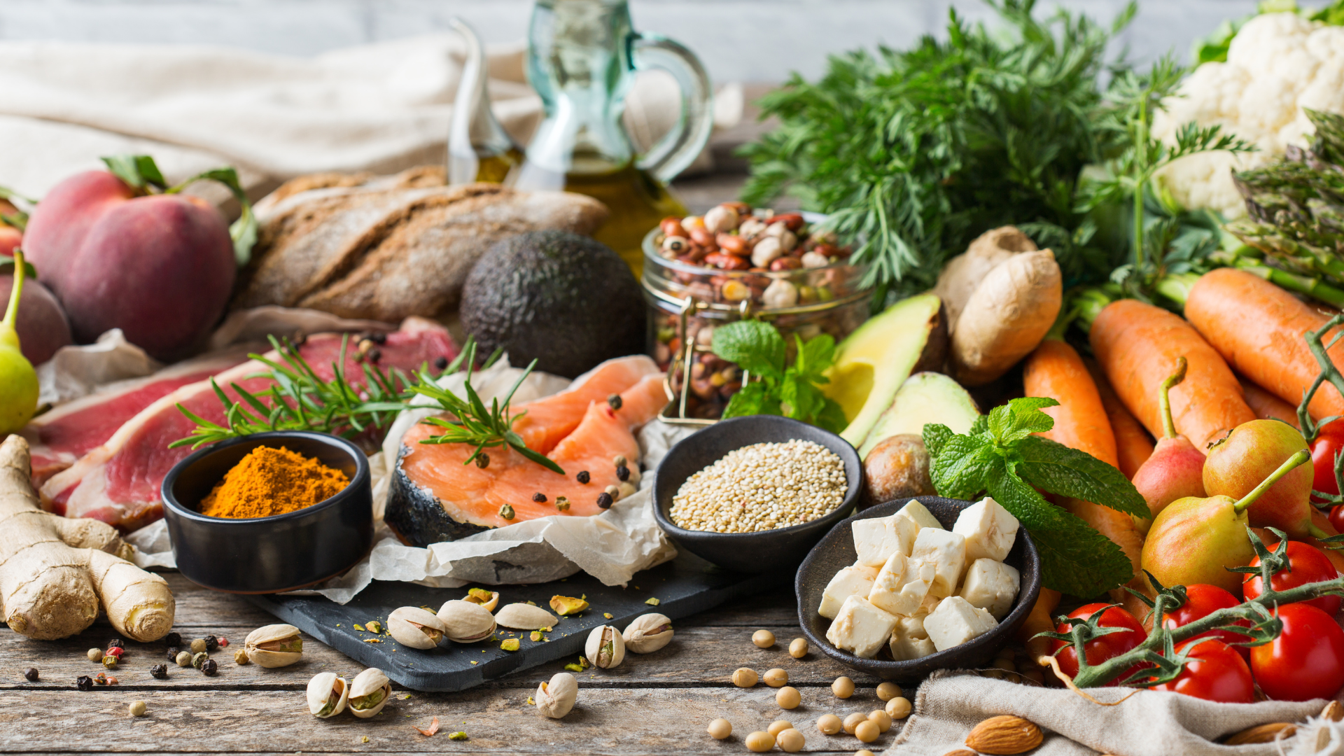 Assorted healthy foods including salmon, vegetables, fruits, and spices on a wooden table.