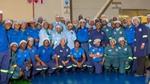Factory employees in uniforms and hairnets pose together on the production floor.