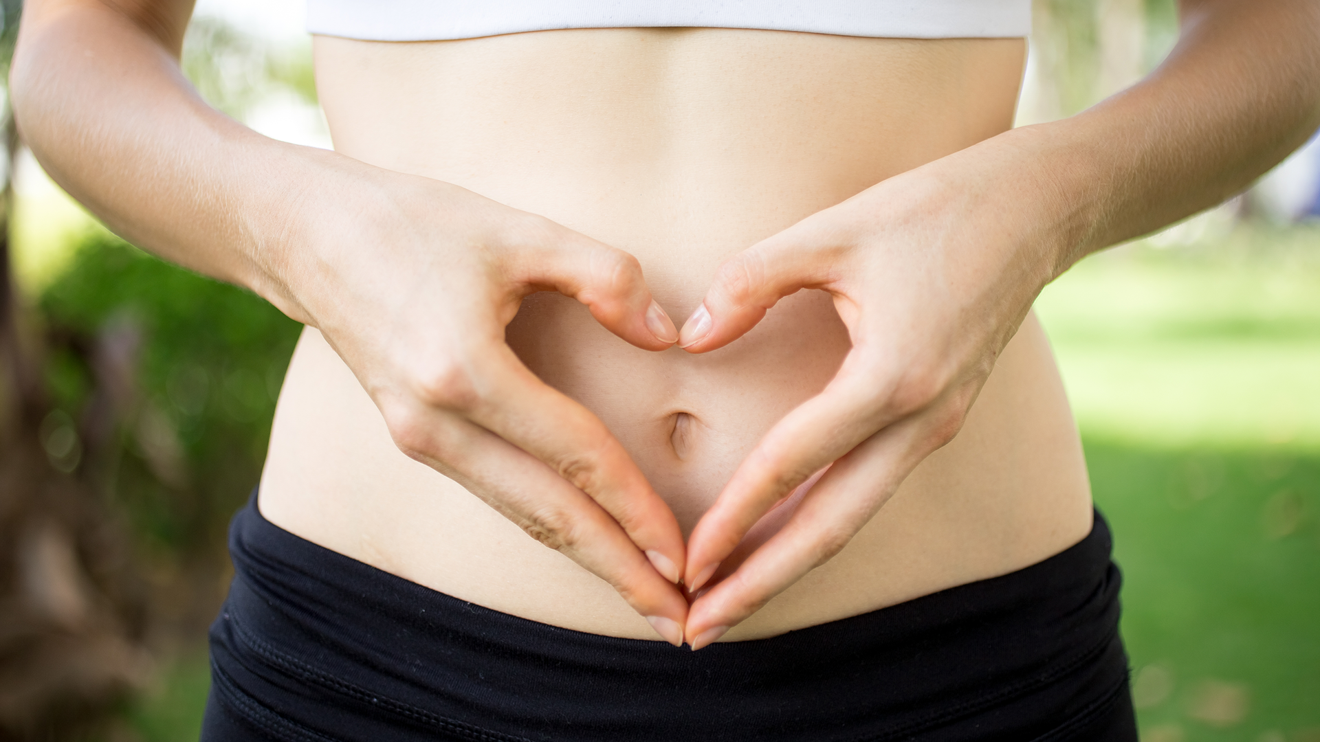 A woman making a heart shape with her hands in front of her gut.