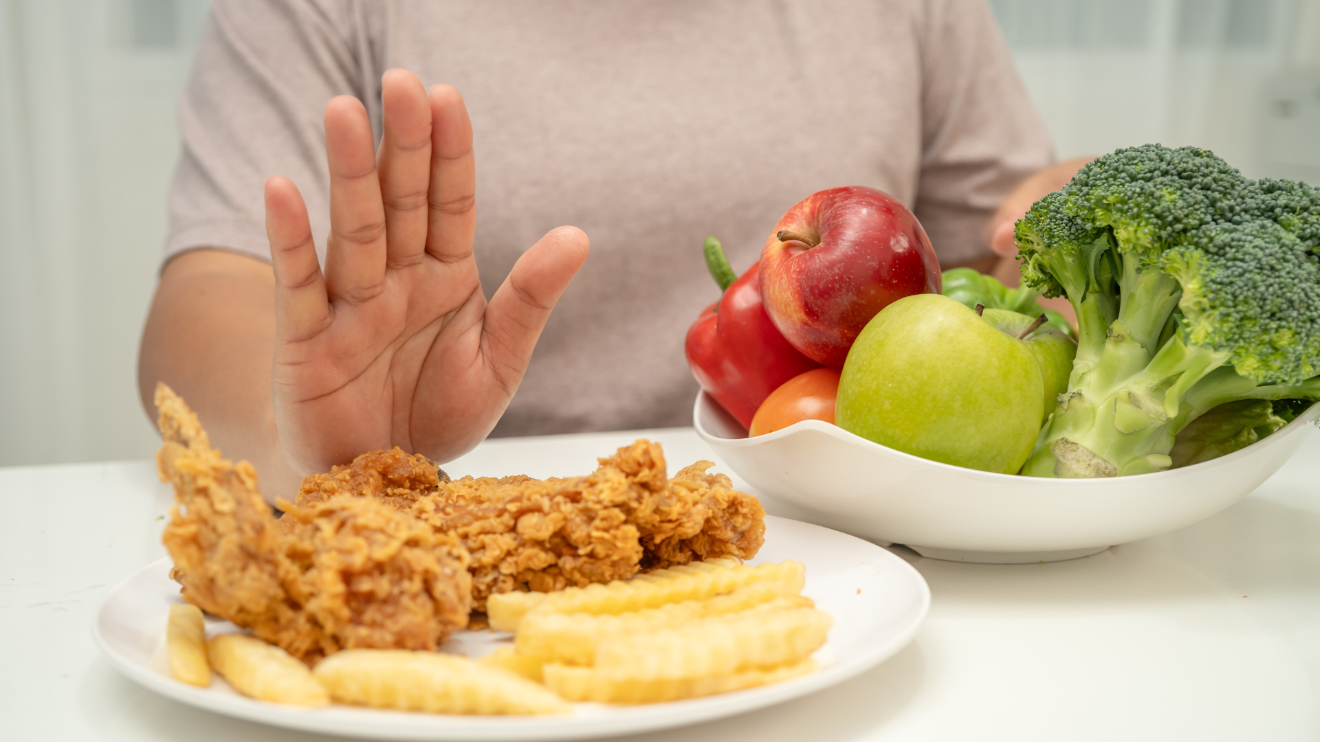 Hand rejecting fried chicken and fries, opting for fruits and vegetables.