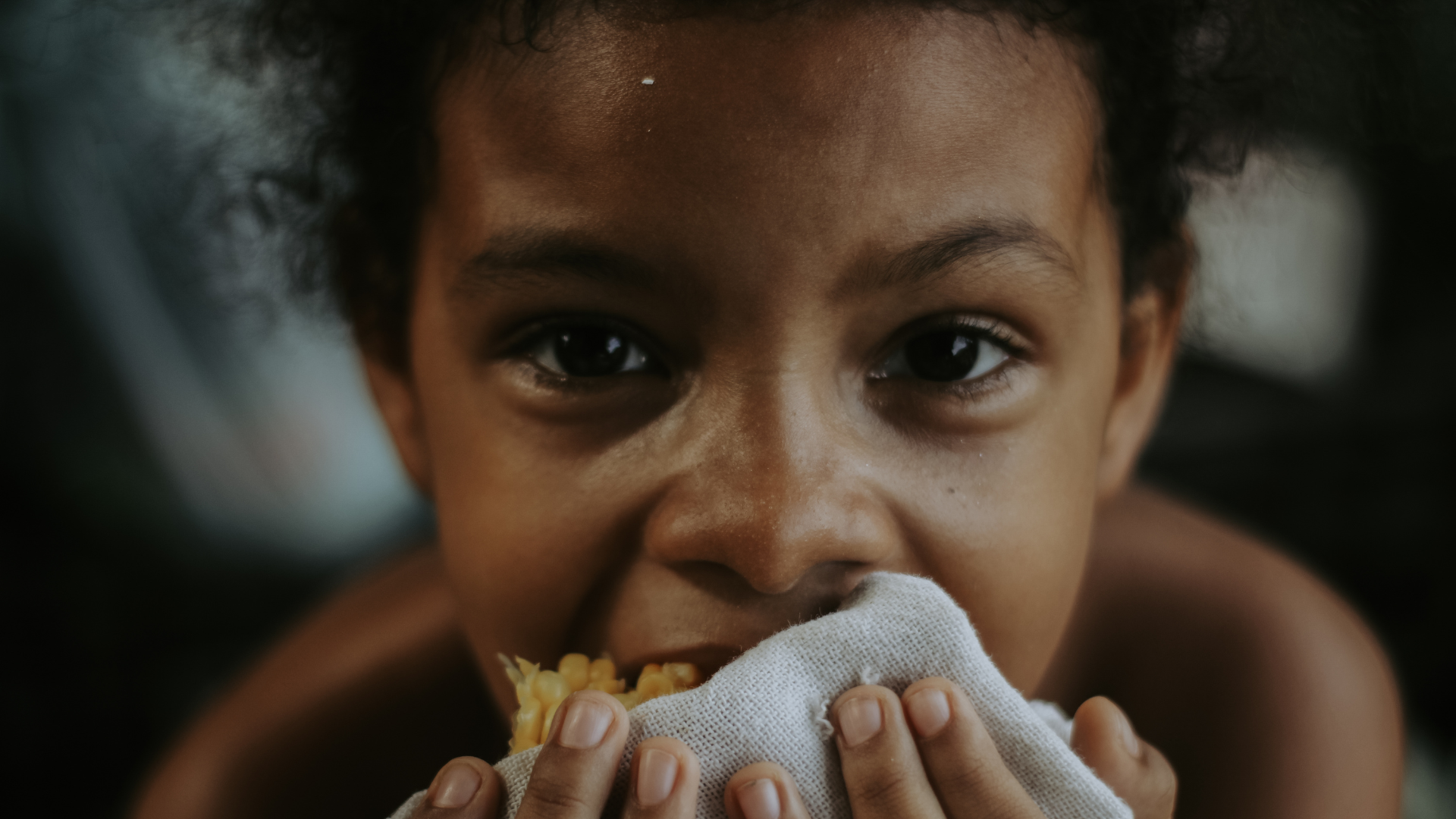 Child eating corn, holding cloth.