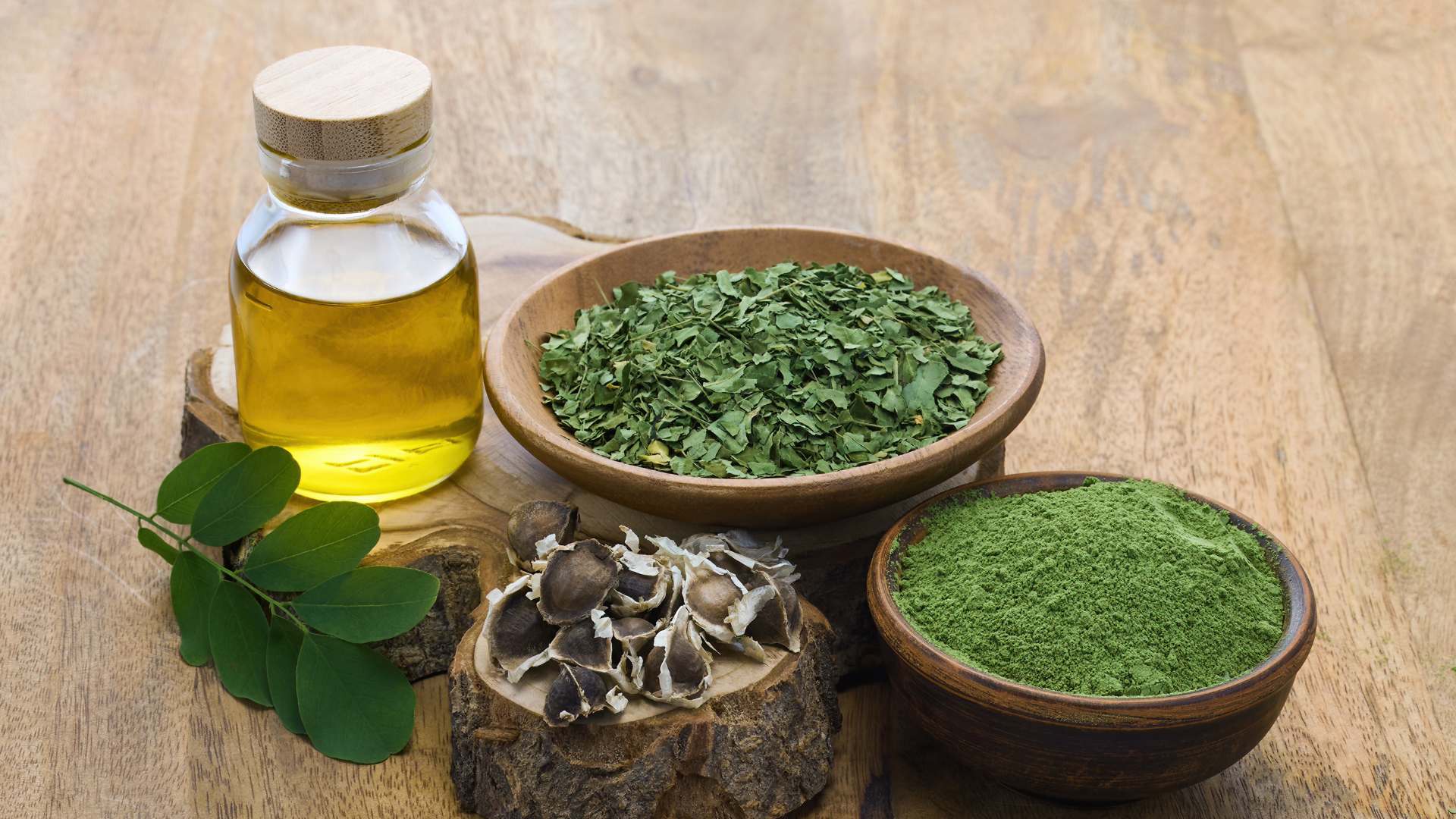 Moringa oil, leaves, seeds, and powder on a wooden table.
