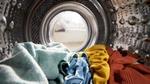 Colourful clothing sitting in the bottom of the drum of a washing machine.