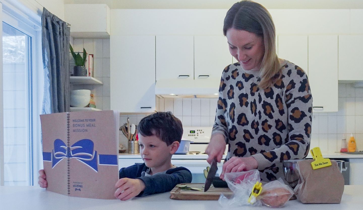 Mother and child in kitchen preparing a meal from a Hellmann’s recipe book.