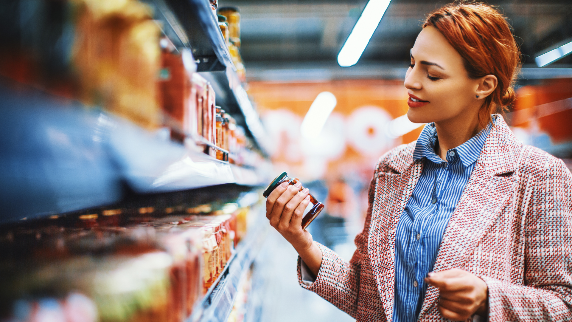 Woman shopping in a grocery store, holding a jar and examining it.