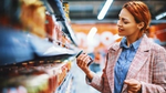 Woman shopping in a grocery store, holding a jar and examining it.