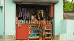 A small shop/kiosk with colourful products displayed on shelves, and a person wearing a traditional sari is standing at the counter.