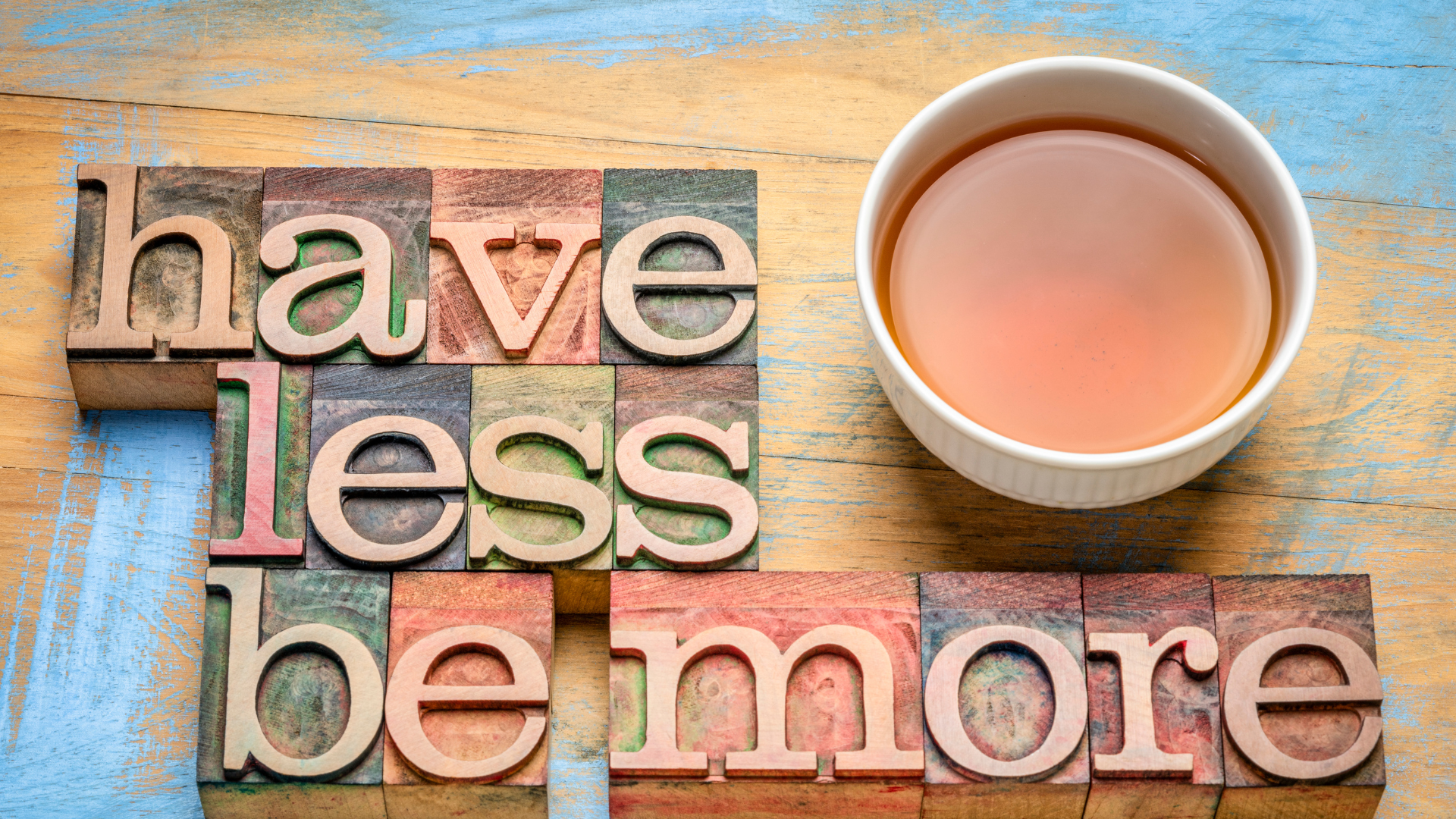 Wood blocks spell 'have less be more' with a cup of tea.