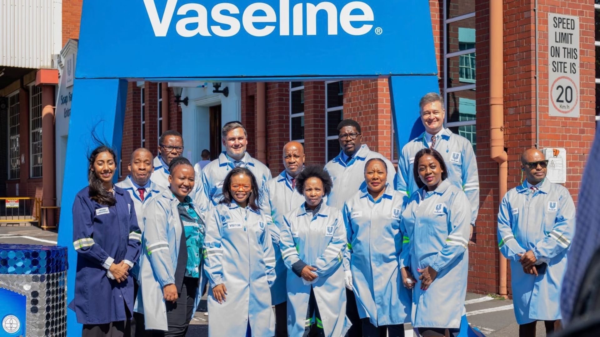 Vaseline factory employees gather beneath a large blue Vaseline sign.