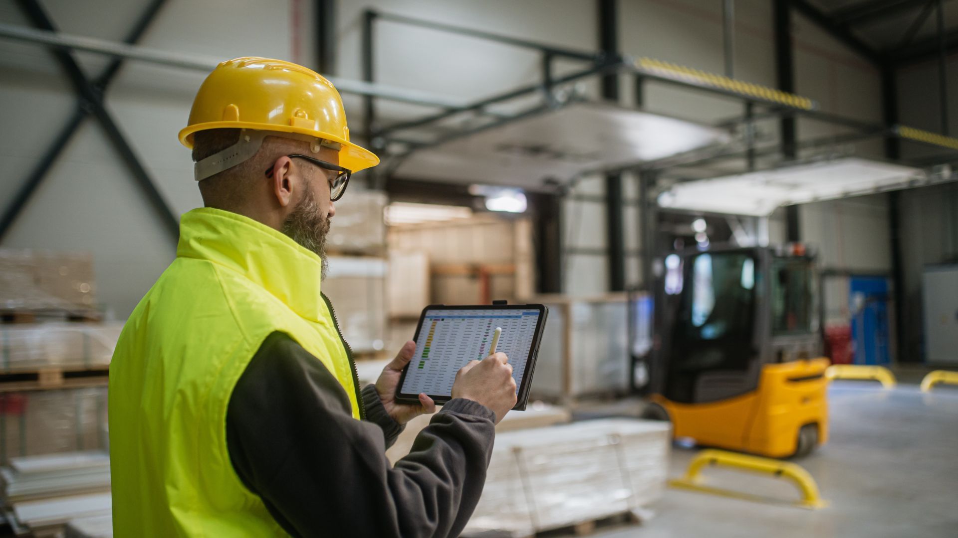 Factory workman wearing protective florescent uniform working on an iPad in a manufacturing warehouse.