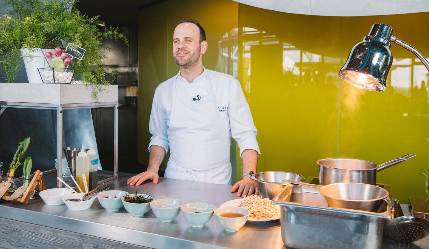 Michelin-starred chef Gregory Marchand stands behind a kitchen worktop bowls of a variety of ingredients