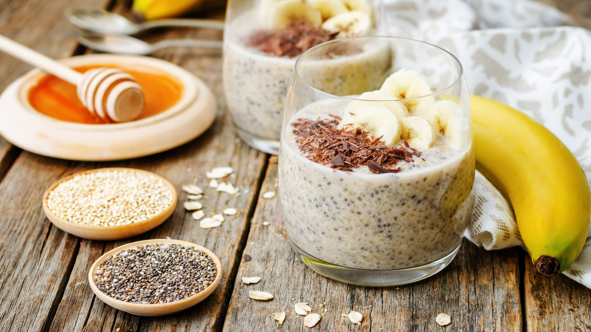 Two cups with chia seed puddings, next to a banana, chia seeds and honey.