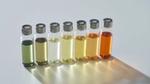 Eight small glass vials containing liquids of varying colors, ranging from green to orange, arranged in a row on a light surface.