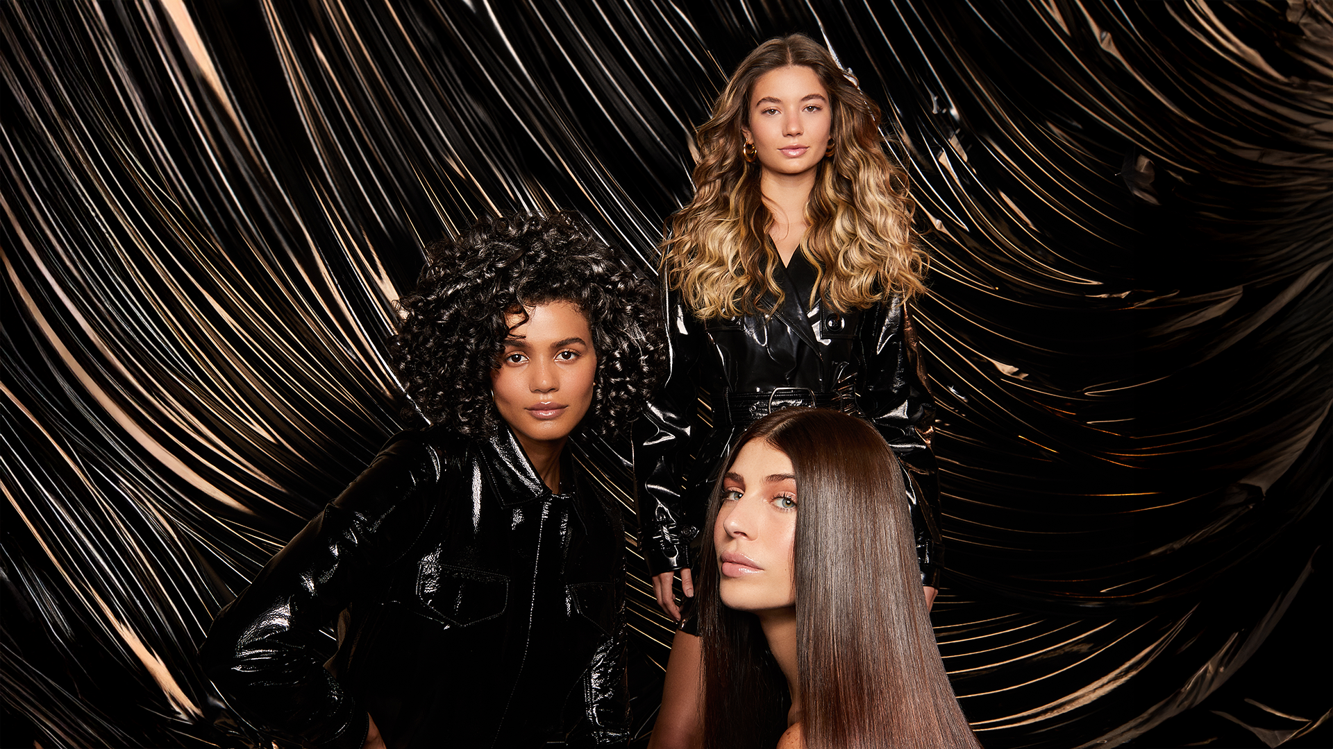 Three women with shiny hair, one blonde waves, one dark curls, one dark glossy. Photo is an ad for TRESemmé Lamellar Shine.