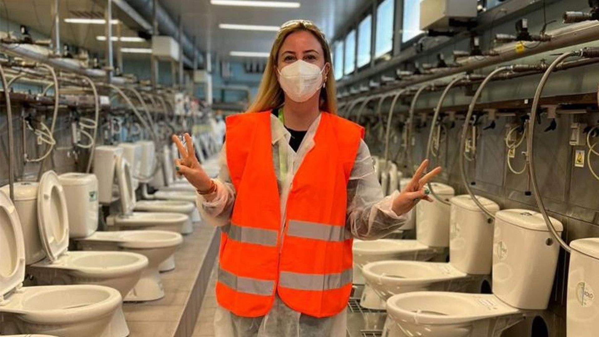Deniz standing in front of a row of toilets in a warehouse.