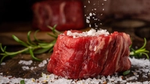 Raw steak with coarse salt and rosemary on a wooden surface.