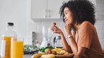 Woman enjoying fruit at kitchen counter with juice and blender.
